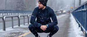 Ein Mann sitzt in der Hocke, während es schneit. 