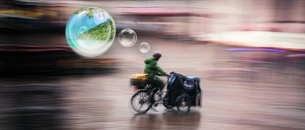 Ein Mann fährt an einem regnerischen und windigen Tag mit dem Lastenrad – und träumt von Urlaub.