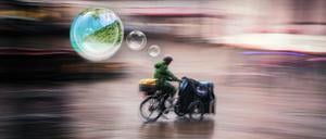 Ein Mann fährt an einem regnerischen und windigen Tag mit dem Lastenrad – und träumt von Urlaub.