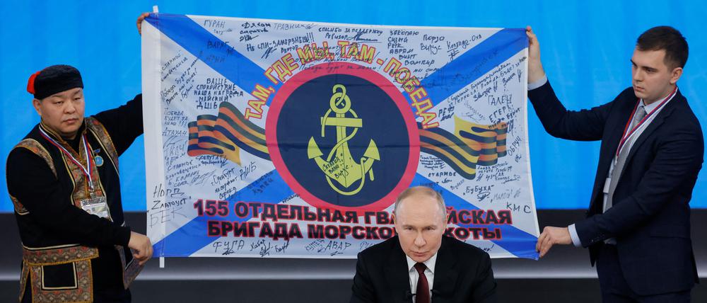 Putin präsentiert während der Pressekonferenz Geschenke von russischen Soldaten, hier eine unterschriebene Flagge von Angehörigen der Pazifikflotte.