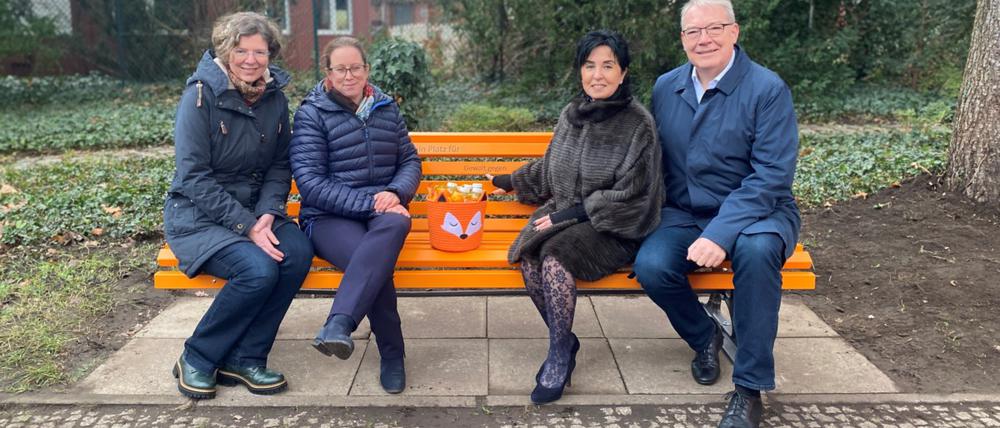 Stadträtinnen Korinna Stephan (Grüne), Julia Schrod-Thiel, Bürgermeisterin Emine Demirbüken-Wegner, Stadtrat Harald Muschner (alle drei CDU, von links nach rechts) auf einer orangefarbenen Bank, die gegen Gewalt an Frauen und Mädchen sensibilisieren soll.