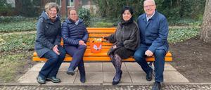Stadträtinnen Korinna Stephan (Grüne), Julia Schrod-Thiel, Bürgermeisterin Emine Demirbüken-Wegner, Stadtrat Harald Muschner (alle drei CDU, von links nach rechts) auf einer orangefarbenen Bank, die gegen Gewalt an Frauen und Mädchen sensibilisieren soll.