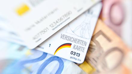 Versichertenkarten verschiedener Krankenkassen liegen auf Geldscheinen. 
 
