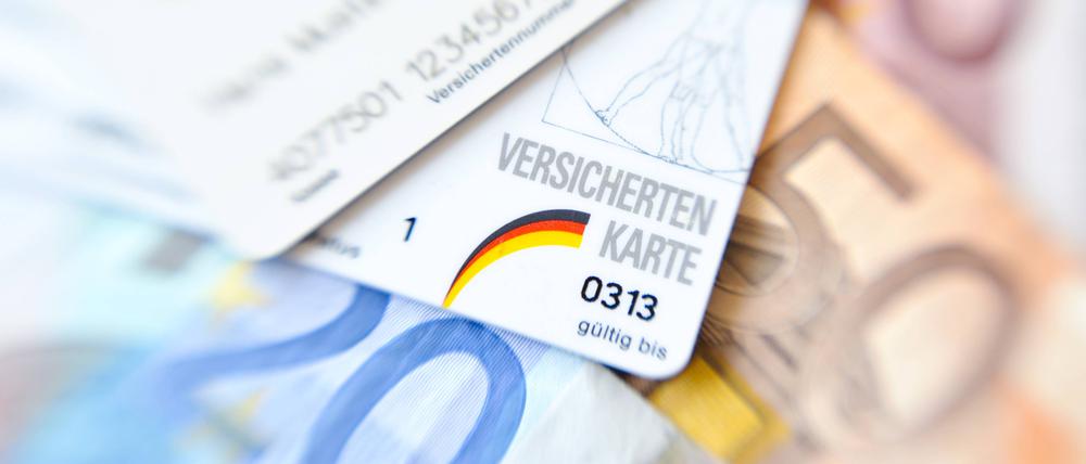 Versichertenkarten verschiedener Krankenkassen liegen auf Geldscheinen. 
 