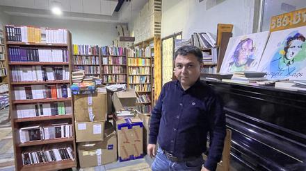 Jehat Rojhilat vor dem verstimmten Klavier im Buchladen, auf dem Porträts bekannter kurdischer Dichter und Sänger stehen.