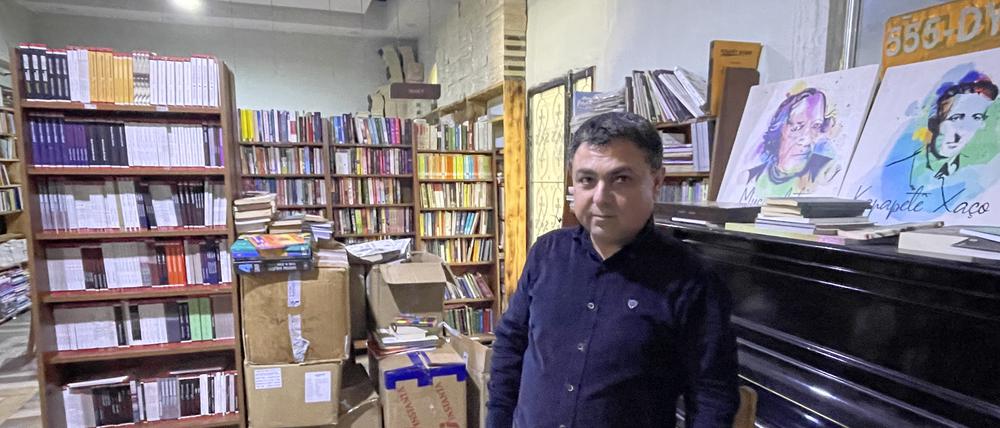 Jehat Rojhilat vor dem verstimmten Klavier im Buchladen, auf dem Porträts bekannter kurdischer Dichter und Sänger stehen.
