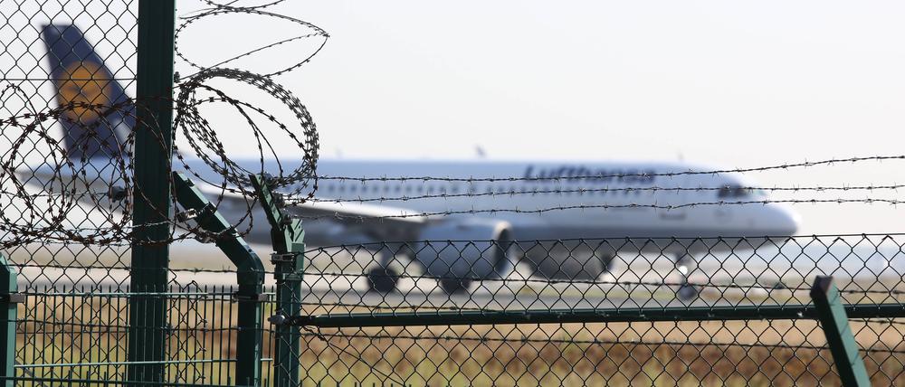 Symbolfoto zum Thema Abschiebung: Ein Flugzeug der Fluggesellschaft Lufthansa startet auf dem Flughafen Frankfurt a.M., im Vordergrund ein Sicherheitszaun mit Stacheldraht.