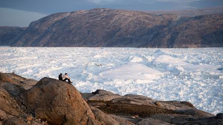 Zwei Studenten der New York University sitzen auf einem Felsen mit Blick auf den grönländischen Helheim-Gletscher. 