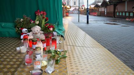 Kerzen, Kuscheltiere und Blumen stehen auf dem Boden an einem Stand auf dem Weihnachtsmarkt.