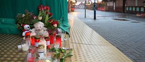 Kerzen, Kuscheltiere und Blumen stehen auf dem Boden an einem Stand auf dem Weihnachtsmarkt.