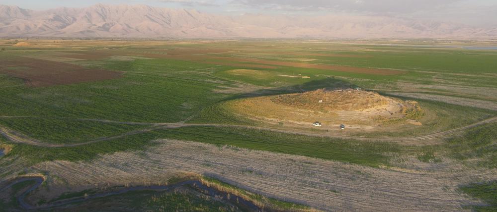 Luftbild des archäologischen Fundortes Gird-i Shamlu im Vordergrund bei laufenden Grabungen. Im Hintergrund das Zagros-Gebirge an der irakisch-iranischen Grenze.