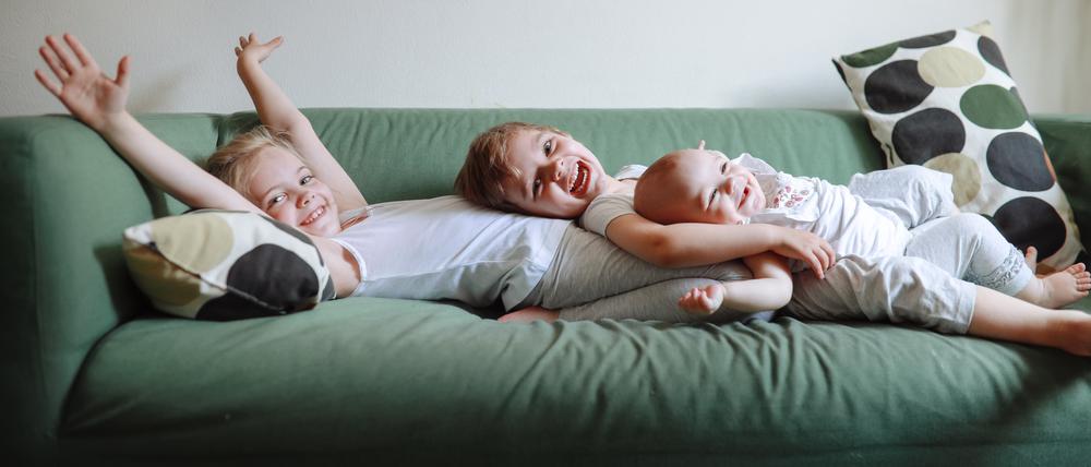 Drei kleine Geschwisterkinder liegen auf einem Sofa. 