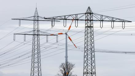 Ein Windrad steht neben dem Mast einer Hochspannungsleitung und dreht sich im Wind. 