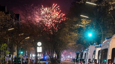 31.12.2024, Berlin: Fahrzeuge der Polizei stehen in der Sonnenallee im Stadtbezirk Neukölln in der Verbotszone für Feuerwerk. Im Hintergrund außerhalb der Zone ist am Himmel Feuerwerk zu sehen. Foto: Soeren Stache/dpa +++ dpa-Bildfunk +++