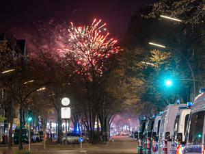 31.12.2024, Berlin: Fahrzeuge der Polizei stehen in der Sonnenallee im Stadtbezirk Neukölln in der Verbotszone für Feuerwerk. Im Hintergrund außerhalb der Zone ist am Himmel Feuerwerk zu sehen. Foto: Soeren Stache/dpa +++ dpa-Bildfunk +++