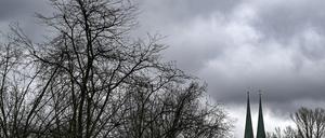 Die Türme von der Nikolaikirche und kahle Bäume bei trübem Wetter und Regenwolken.
