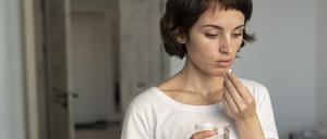 Eine junge Frau hält eine Tablette in der einen, ein Glas Wasser in der anderen Hand.