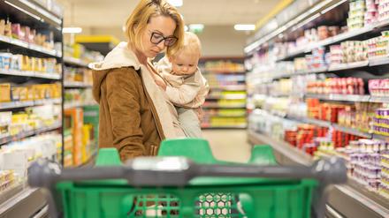Mutter mit Baby auf dem Arm im Supermarkt.