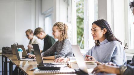 Studierende sitzen im Unterricht in der Uni, zwei Frauen schauen gut gelaunt auf ihre Laptops (Symbolbild).