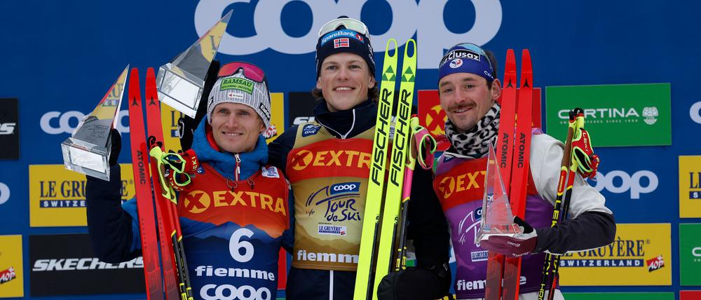 Johannes Hoesflot Klaebo (M) aus Norwegen jubelt neben dem Zweitplatzierten Mika Vermeulen (l) aus Österreich und dem Drittplatzierten Hugo Lapalus aus Frankreich auf dem Podium der Tour de Ski.