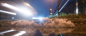 Autos fahren hinter einem kleinen Rest Schnee vorbei, der sich in einer Pfütze spiegelt.