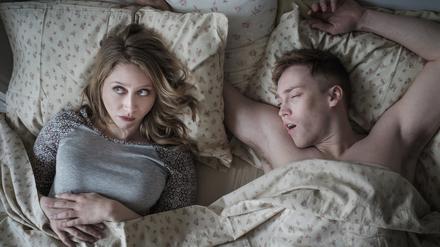 Eine wache junge Frau im Bett neben einem schlafenden Mann.
