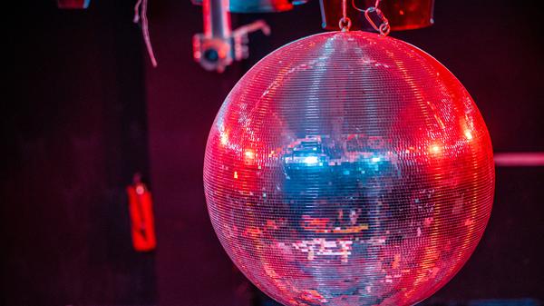 Eine farbig beleuchtete Discokugel dreht sich über der Tanzfläche. (Symbolbild)