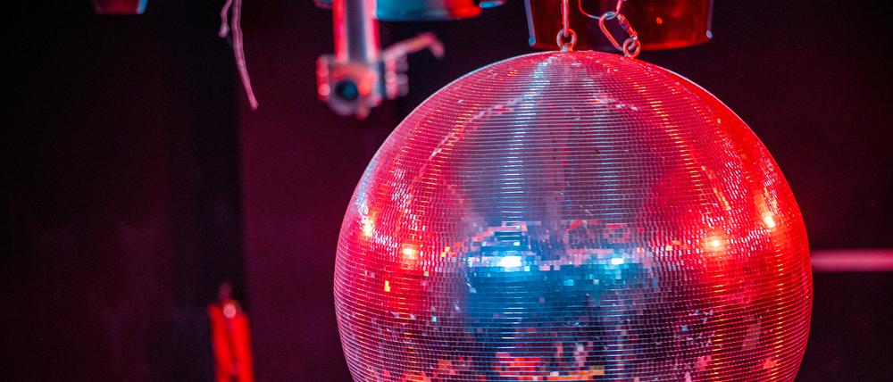 Eine farbig beleuchtete Discokugel dreht sich über der Tanzfläche. (Symbolbild)