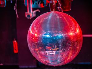 Eine farbig beleuchtete Discokugel dreht sich über der Tanzfläche. (Symbolbild)
