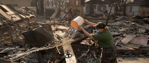 Eine Frau gießt Wasser auf das vom Feuer verwüstete Grundstück eines Nachbarn nach dem Palisades-Brand im Stadtteil Pacific Palisades von Los Angeles. 