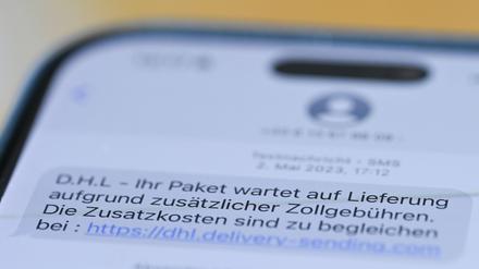 Auf einem Smartphone ist eine Betrugs-SMS zu lesen, in der Kriminelle ein Paket ankündigen und dafür Zollgebühren einfordern. 