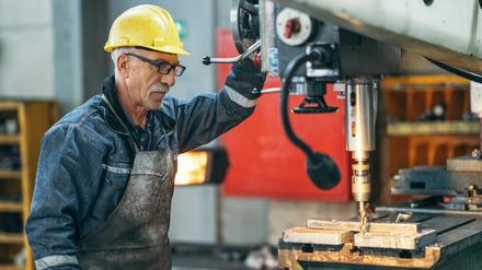 Ein älterer Mann arbeitet in einer Werkstatt an einer Maschine. 