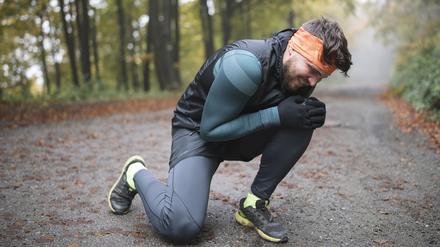 Ein junger Jogger greift sich mit schmerzverzerrtem Gesicht ans linke Knie.