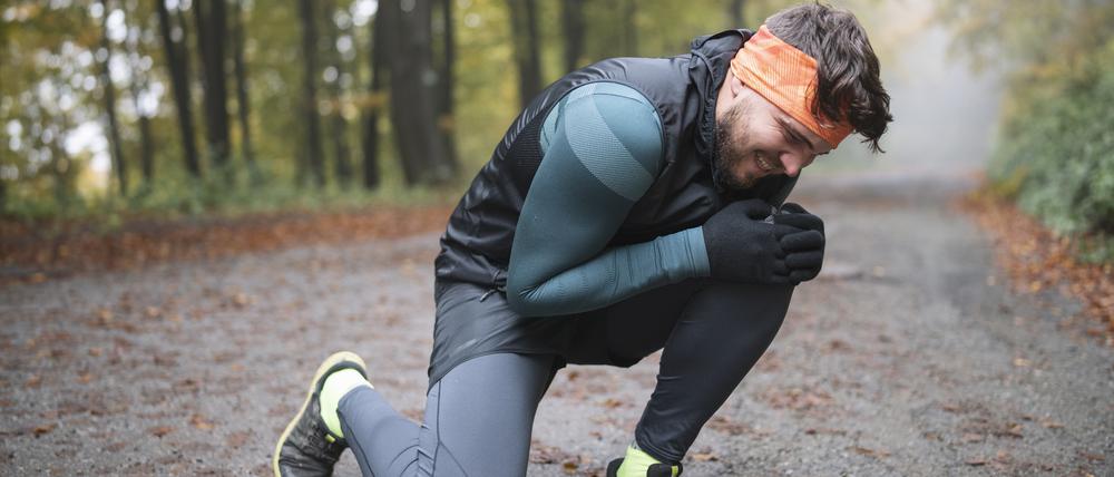 Ein junger Jogger greift sich mit schmerzverzerrtem Gesicht ans linke Knie.