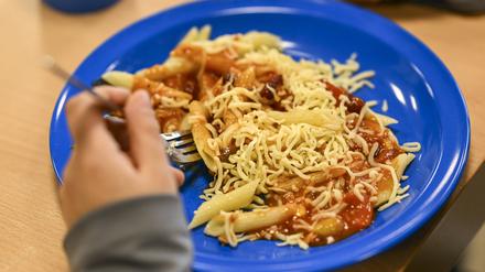 Ein Kind hat beim Schulessen Nudeln mit Tomatensoße und geriebenem Käse auf dem Teller.