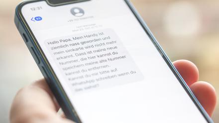 Eine Frau hält ein Smartphone in ihrer Hand, auf dessen Display eine Betrugs-SMS zu lesen ist.