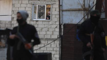 Eine Frau schaut aus dem Fenster ihres Hauses, während Sicherheitskräfte, die der syrischen Übergangsregierung unterstellt sind: Konflikte wie der über Jahre in Syrien sind für die Weltwirtschaft aus Expertensicht das aktuell größte Risiko: 