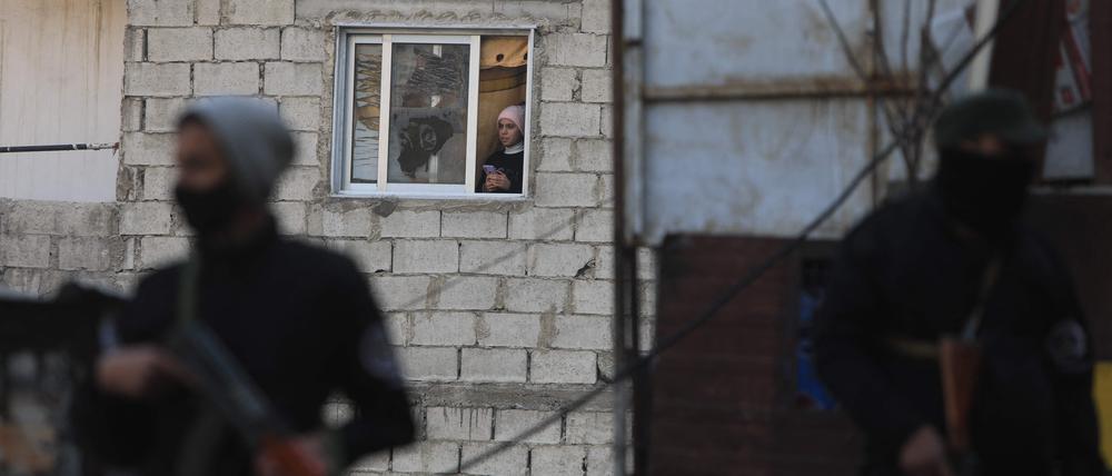 Eine Frau schaut aus dem Fenster ihres Hauses, während Sicherheitskräfte, die der syrischen Übergangsregierung unterstellt sind: Konflikte wie der über Jahre in Syrien sind für die Weltwirtschaft aus Expertensicht das aktuell größte Risiko: 