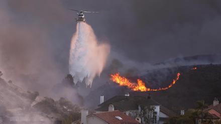 Ein Helikopter wirft am 7. Januar Wasser auf vom Palisades Feuer bedrohte Häuser in Los Angeles.  Nachlassende Winde könnten die Lage in den Waldbrandgebieten bald deutlich verbessern. 