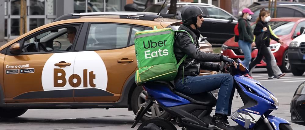 Ein Uber Eats-Kurier auf dem Roller und ein Auto mit Bolt-Logo im Hintergrund.