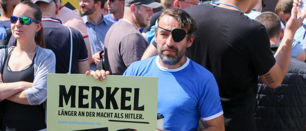 Liebich 2019 mit einem Plakat, das Angela Merkel in eine Reihe mit Adolf Hitler stellt.