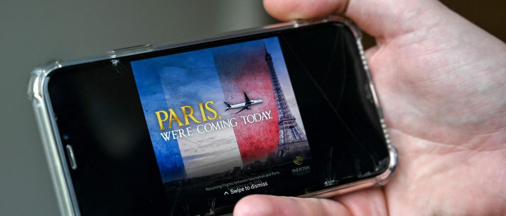 Ein Mann sieht sich auf seinem Handy in Islamabad am 17. Januar 2025 eine Werbung der Pakistan International Airlines (PIA) an, die den Eiffelturm anfliegt. Pakistans umkämpfte nationale Fluggesellschaft entschuldigte sich am 17. Januar für eine Anzeige, die ein Flugzeug beim Anflug auf den Eiffelturm zeigt und anlässlich des ersten Fluges nach Paris nach Aufhebung des Sicherheitsverbots veröffentlicht wurde.