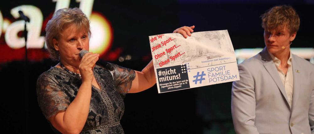 Stadtsportbund-Vorsitzende Ute Goldberg hält ein kleines Plakat gegen die Sparpläne der Stadt in die Höhe, daneben steht Moderator und Olympia-Gewinner Jacob Schopf.