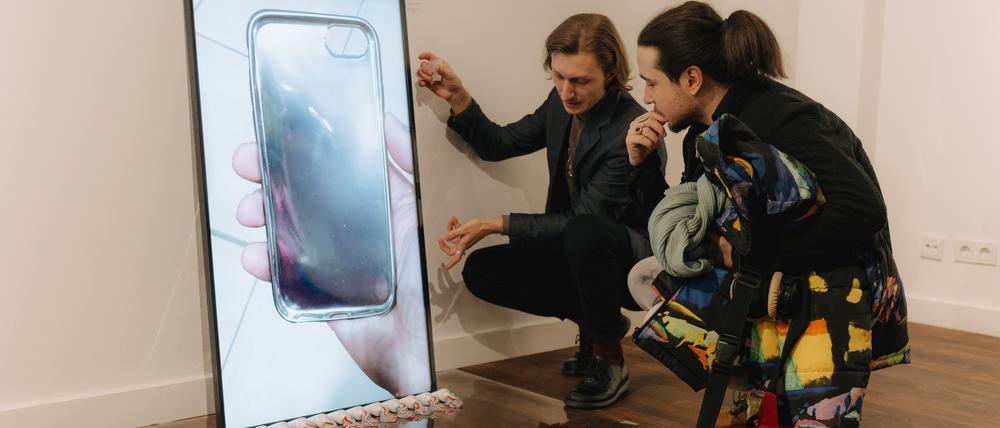 Der Künstler Vitalii Shupliak (lks.) erklärt einem Besucher sein 2020 entstandenes Video „Hypertonie“. Der Bildschirm steht auf geöffneten Zahnpastatuben.