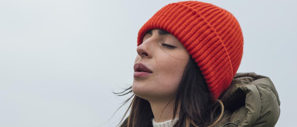 Eine junge Frau in Winterkleidung holt tief Luft.