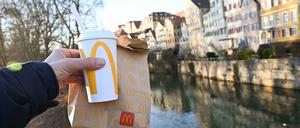 Eine McDonald’s To-Go-Tüte und ein To-Go-Becher werden auf der Neckarbrücke in Tübingen vor der Kulisse der Altstadt gehalten (gestellte Szene).