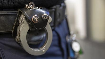 Eine Handschelle hängt am Gürtel eines Polizisten.