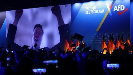 Elon Musk (l) auf einem großen Bildschirm bei der AfD-Wahlkampfshow am 25. Januar 2025 in Halle. Rechts vorne steht Alice Weidel.