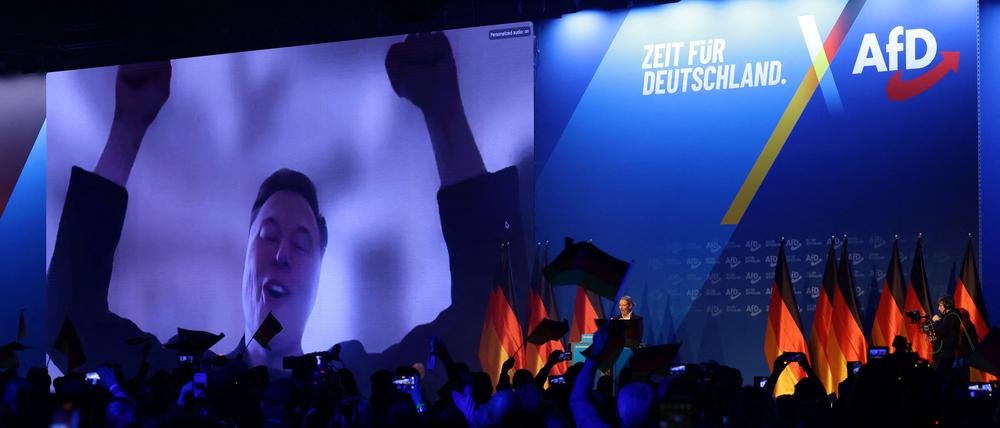 Elon Musk (l) auf einem großen Bildschirm bei der AfD-Wahlkampfshow am 25. Januar 2025 in Halle. Rechts vorne steht Alice Weidel.