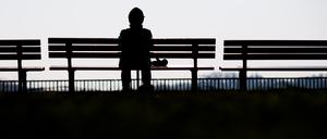 Eine Frau sitzt allein auf einer Bank in der Sonne.